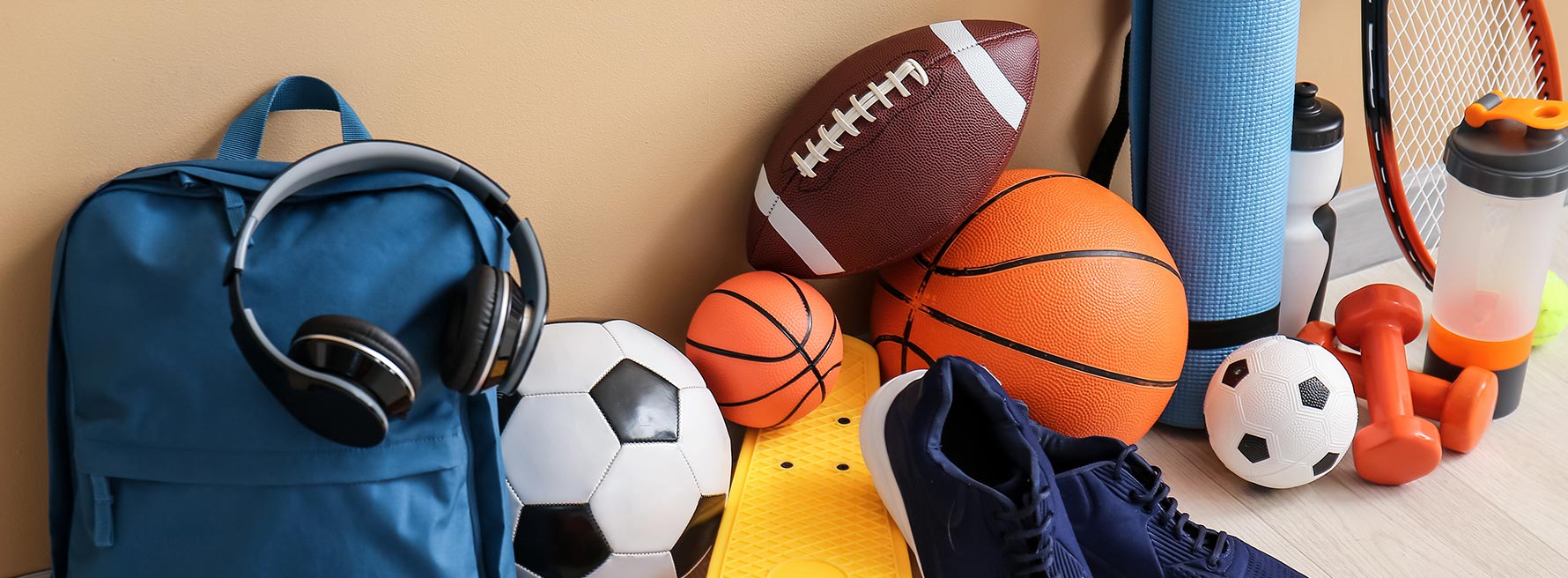 Sports gear including a soccer ball, football, basketballs & skateboard, sneakers and a blue backpack.