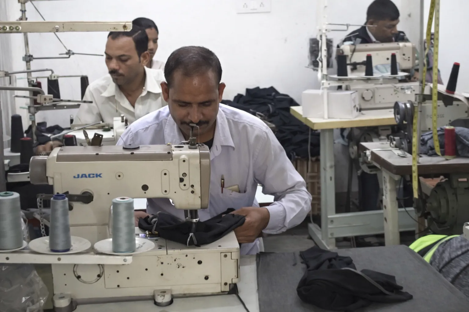 Workers operating sewing machines in a garment factory, stitching fabric pieces in a clothing production workshop.