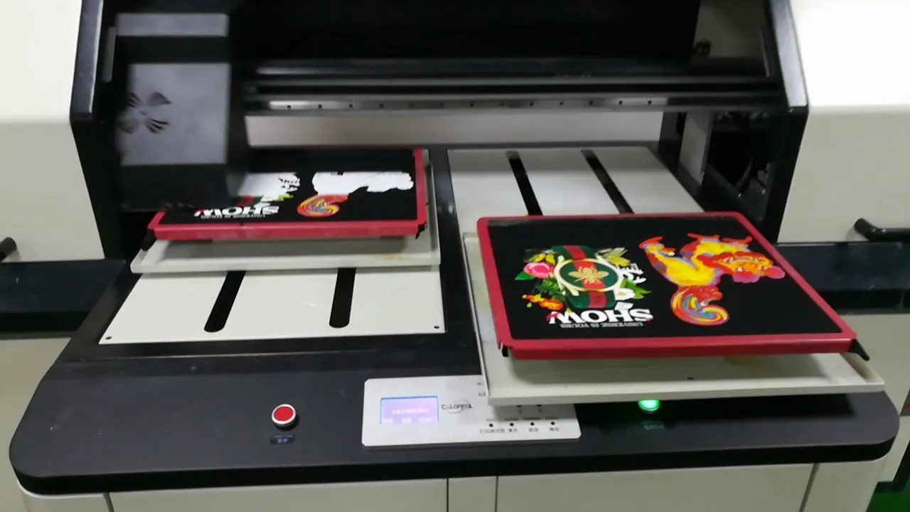 A digital printing machine producing custom printed T-shirts with colorful designs on fabric sheets in a manufacturing setup.