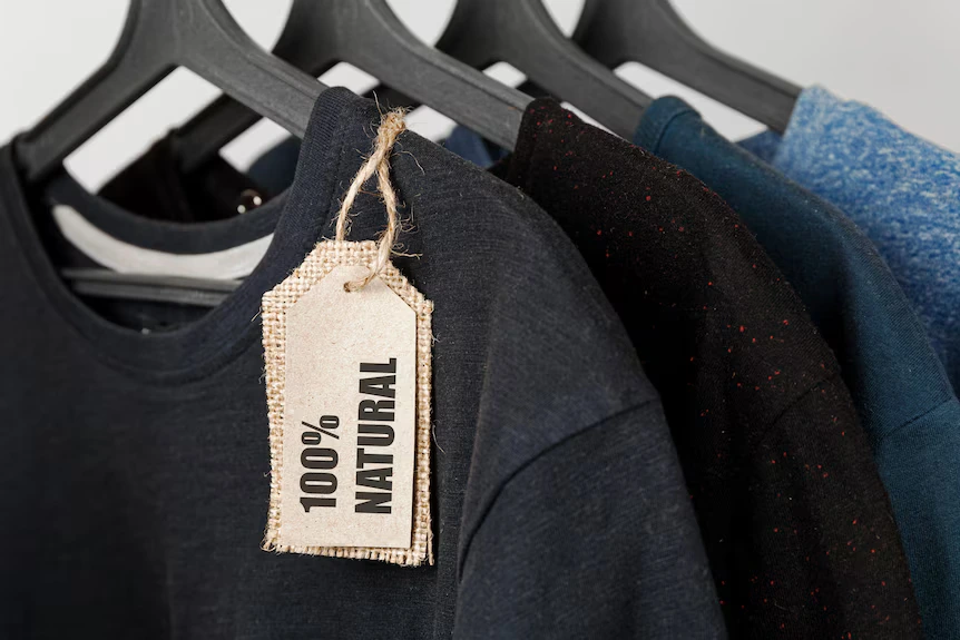 100% natural cotton t-shirts hanging on black hangers with eco-friendly fabric tag.