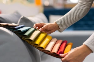 Hands selecting colorful fabric swatches for textile and clothing design, showing material and color options for garment production.
