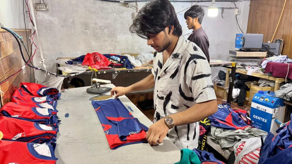 Worker folding custom red and blue sports jerseys at an apparel manufacturing facility.