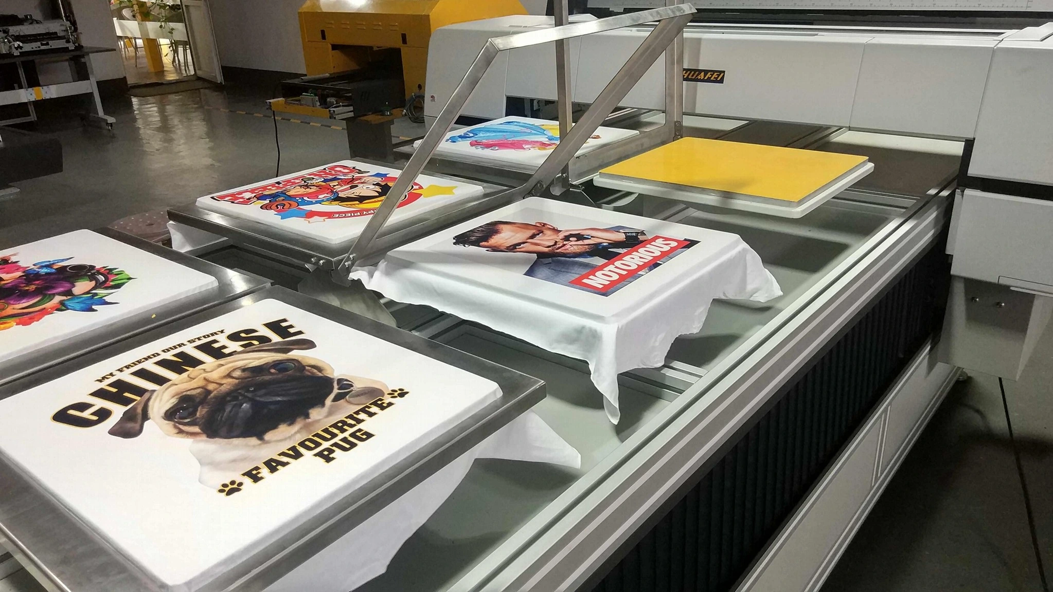 Industrial DTG printing machine printing colorful custom graphics on multiple white t-shirts at the same time.