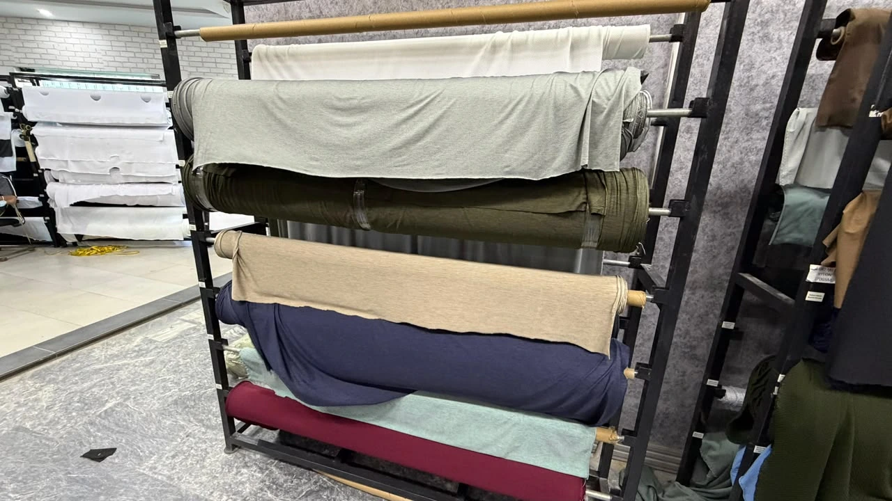 Premium cotton fabric rolls in assorted colors displayed on a textile rack for garment and clothing manufacturing.